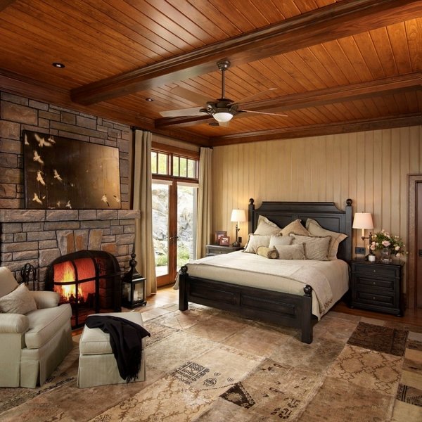rustic bedroom decor stone fireplace design ideas wooden ceiling black headboard upholstered armchair