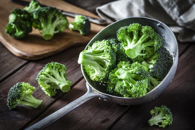 broccoli florets in a ladle on wooden table