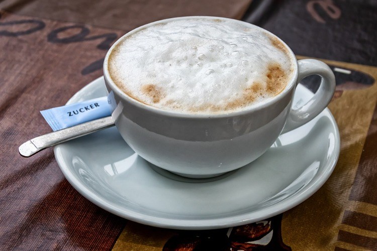 cappuccino with foam in white cup with saucer and sugar