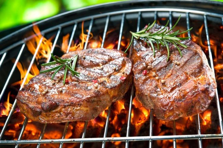 grilled steaks with rosemary on the grid and flames from the coals