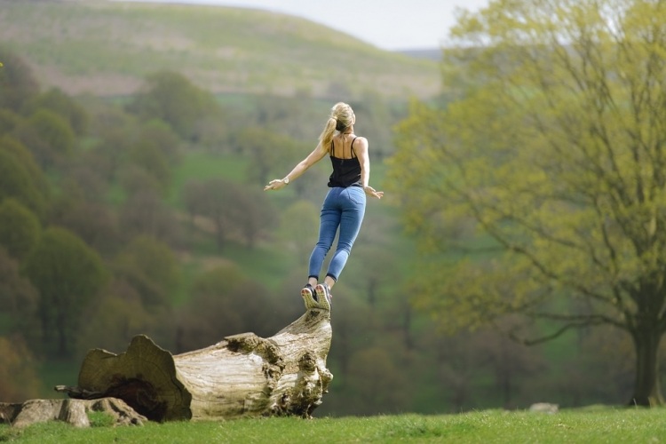 blonde woman in jeans on a tree trunk jumping in the air