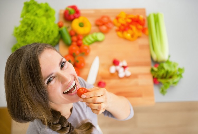 smiling woman eats cherry tomato vegetables on cutting board in the background