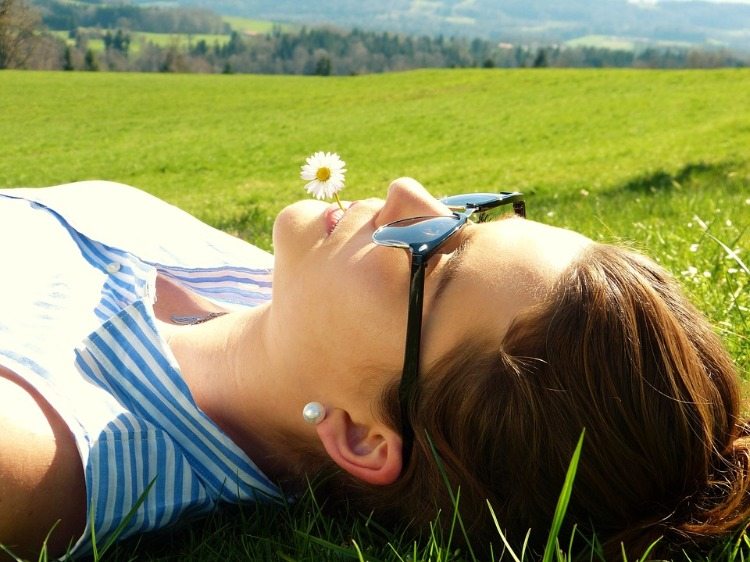 woman with sunglasses holds white flower in mouth under the sun rays