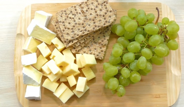 brie and emmental with crackers and grapes on kitchen board as party snacks