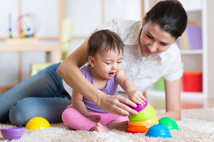 mother and small baby playing on the floor with colorful toys