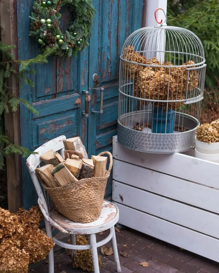 Vintage birdcage with hydrangea and wooden logs as fall decoration for the doorway