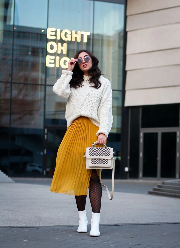 Combining white ankle boots with a pleated skirt is modern and elegant