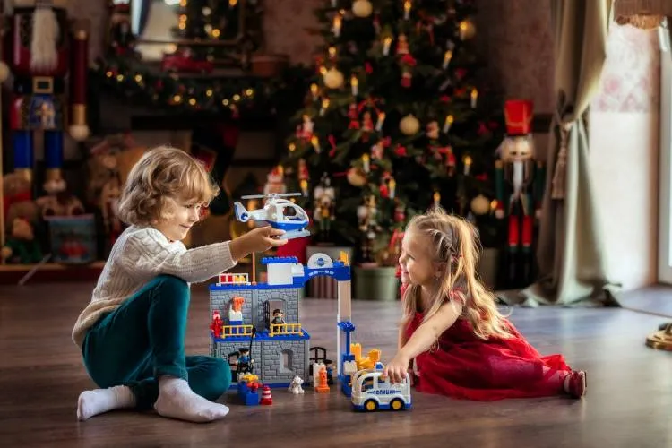 children playing on the floor near a Christmas tree toys presents helicopter police car constructor