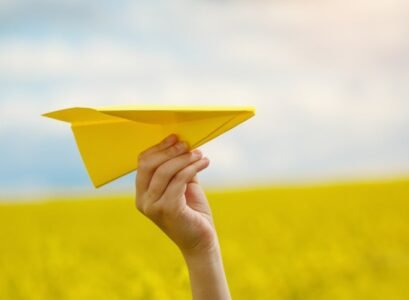 Paper airplane in children hands on yellow background and blue s