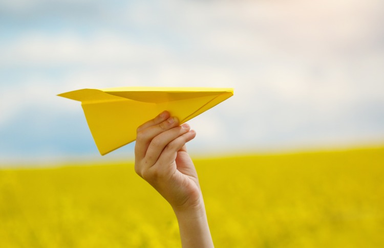 Paper airplane in children hands on yellow background and blue s