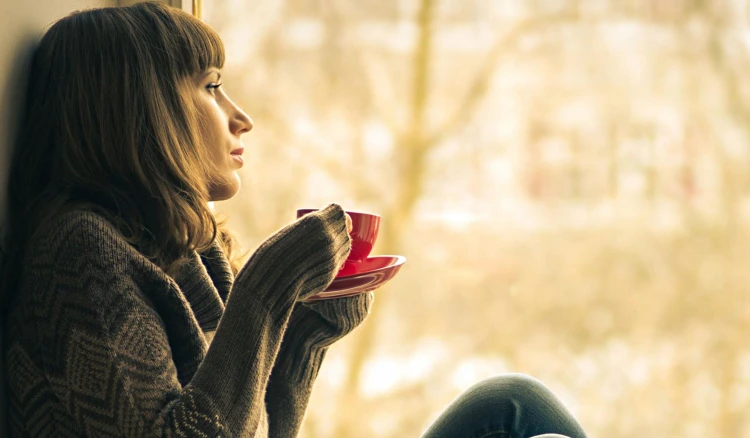 girl sitting on the windowsill thinking and drinking coffee