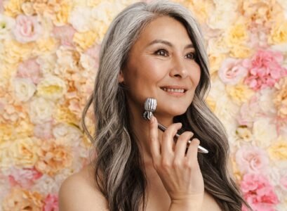 Mature woman massaging face with jade roller standing