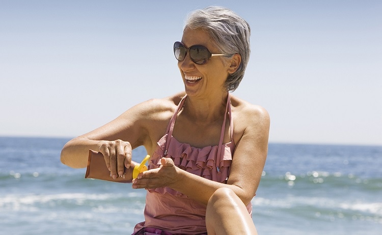 hispanic woman applying sunscreen on beach