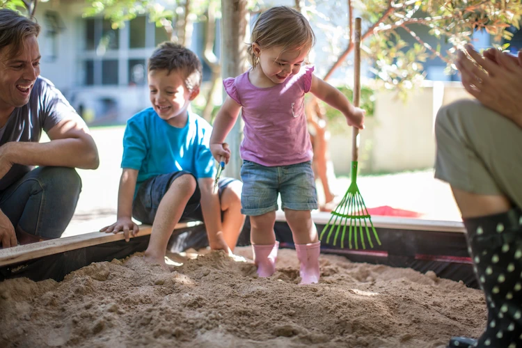 happy family with children playing in a sandbox in summer weather