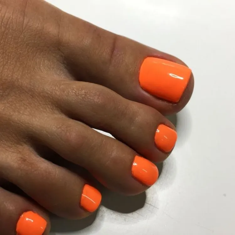 trendiest pedicure color july summer 2023 orange nail polish tan skin