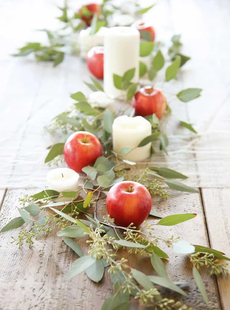 simple fall table centerpiece with apples candles and greenenry
