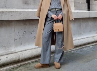 fall office outfit idea styling classic sheepskin ugg boots grey pants zip up sweater long camel coat mini beige handbah grey beanie sunglasses